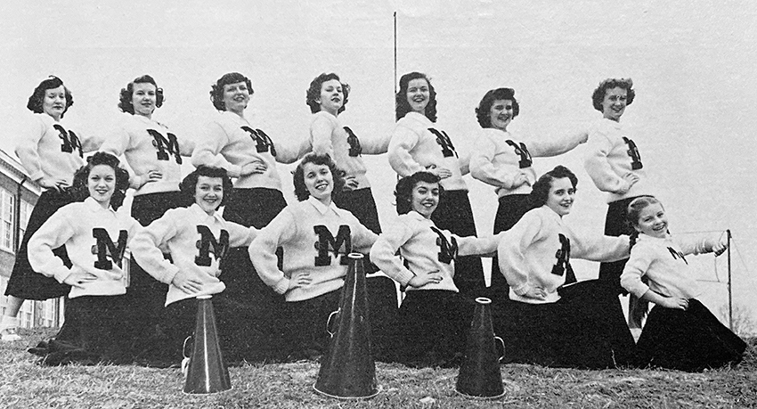 Black and white photograph of the cheerleading squad posed on the field.